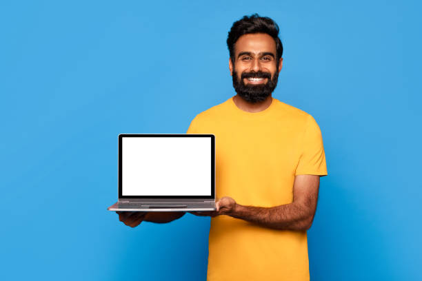 istock Happy indian man in yellow showcasing blank laptop screen 2115159766