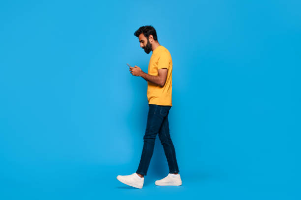 istock Middle aged indian man in yellow walking and texting on phone 2115159775