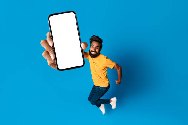 istock Energetic middle aged indian man jumping with phone in hand 2115159783
