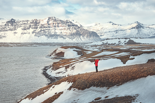 Happy tourist traveler woman wearing red jacket enjoying with open arms in mountain hill in Iceland, Europe travel vacation