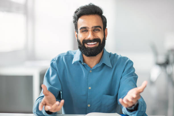 istock Cheerful indian bearded man in blue shirt smiling and gesturing at camera 2115226490
