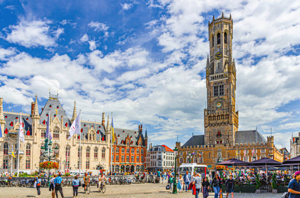Bruges, Belgium, July 5, 2023: people tourists walking down Markt Market square, Belfry of Bruges Belfort van Brugge medieval bell tower, Provincial Court, street restaurants in Brugge old town