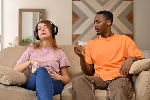 A man is trying to explain something to his girlfriend, who simply puts headphones on her head and ignores attempts at conversation.