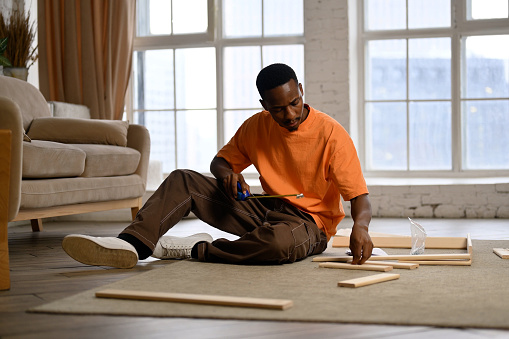Young black man assembling a rack according to instructions at home