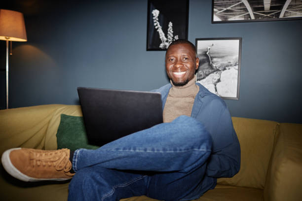 istock Smiling man sitting on couch with laptop 2115291542