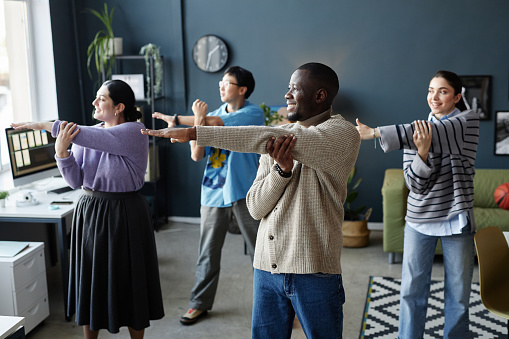 Multiethnic group of cheerful people enjoying stretching exercises at sports break in office