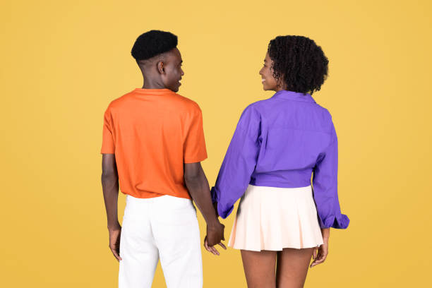 오렌지색 셔츠를 입은 남자와 손을 잡고 있는 젊은 커플의 뒷모습 - purple orange heterosexual couple young men 뉴스 사진 이미지