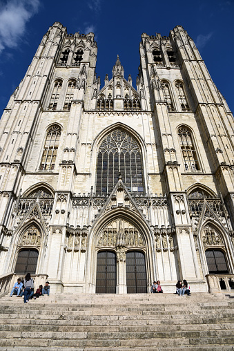 The Cathedral of St. Gudula (Cathedral of St. Michael and St. Gudula) in Brussels. It is a medieval Roman Catholic cathedral in central Brussels, Belgium. The church was built between 11th–15th centuries. The image shows the building exterior with a few people, captured during summer season.