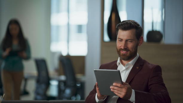 istock Smiling professional swiping tablet computer screen pages at business cabinet 2115358382