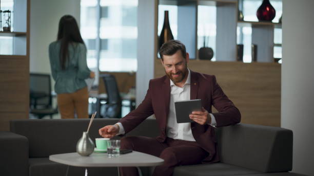 istock Smiling millionaire drinking coffee typing tablet in office. Relax break time 2115379112