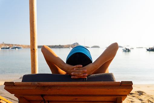 Close up of unknown woman with her arms resting on her head on a sun lounger enjoying a splendid morning on a secluded beach south of the Greek island of Crete