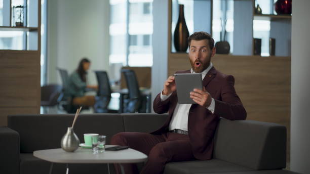 istock Happy businessman shouting yes looking tablet computer screen in big office hall 2115394259