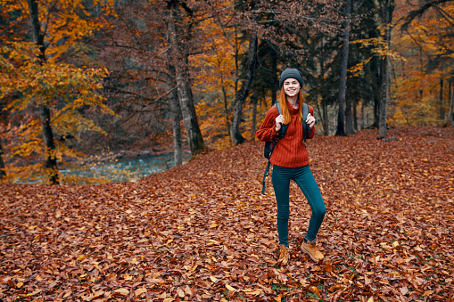 travel tourism and a young woman with a backpack walks in the park in nature landscape tall trees fallen leaves river. High quality photo