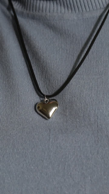 Black choker on a cord with an elegant heart-shaped pendant. On a woman's neck. Vertical video. Close-up.