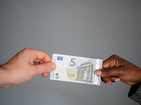 Two multi-racial hands holding a five euro note