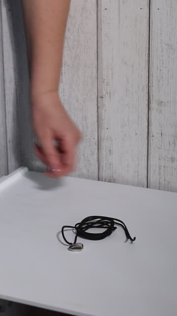 Black choker on a cord with an elegant heart-shaped pendant. A woman reviews his purchase. He rolls it up and puts it on the table. Vertical video.