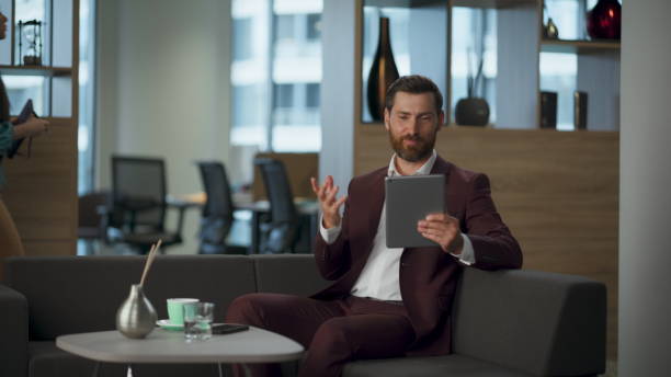 istock Cheerful boss talking video conference at sofa office interior. Man tablet call 2115420186