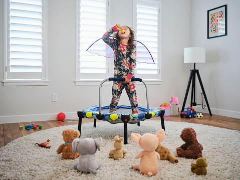 A preschool aged multiracial girl, having a make-believe concert for her toys in a home.