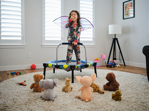 A preschool aged multiracial girl, having a make-believe concert for her toys in a home.