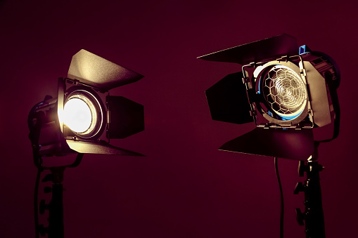 Two cinema projectors with fresnel lens  and barn door limiting curtains. Cinema lights against a burgundy background.