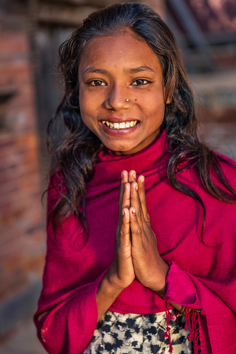Young Nepali girl saying namaste in Bhaktapur. Bhaktapur is an ancient town in the Kathmandu Valley and is listed as a World Heritage Site by UNESCO for its rich culture, temples, and wood, metal and stone artwork.