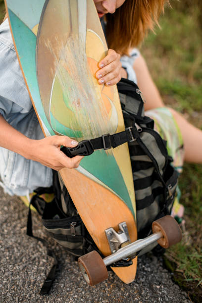 istock girl unfastens her longboard from her backpack, preparing to ride it 2115481969