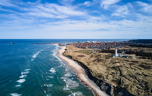 Aerial view of Hirtshals lighthouse and townscape on mountain surrounded with beautiful seascape against cloudy sky on sunny day