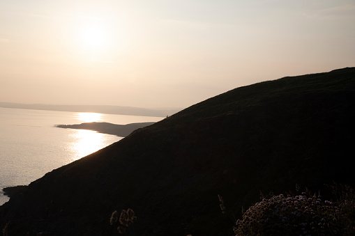 A lone hiker is seen in the distance as he climbs the hill as the sun is setting on the coastline of Ireland