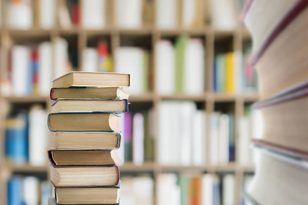 A stack of textbooks against a background of bookshelves in a library.