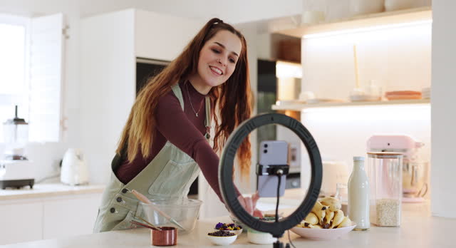 Woman, phone and live streaming in kitchen for food, cooking and meal blog for social media, vlog and website. Happy, lighting or home influencer with mobile technology for baking broadcast tutorial