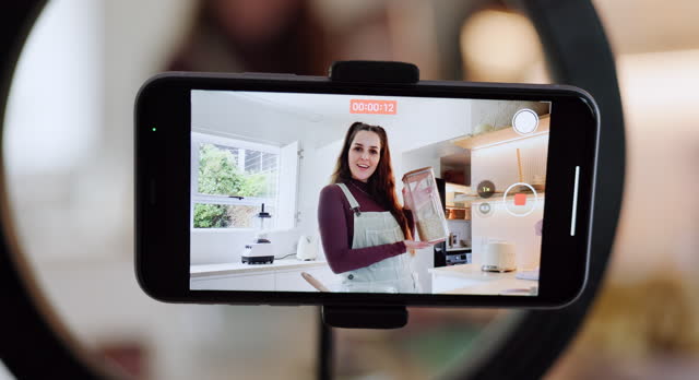 Woman, talking and phone screen for live streaming food, cooking and meal on social media blog, vlog and podcast. Waving hello, greeting or home influencer on technology for kitchen baking tutorial