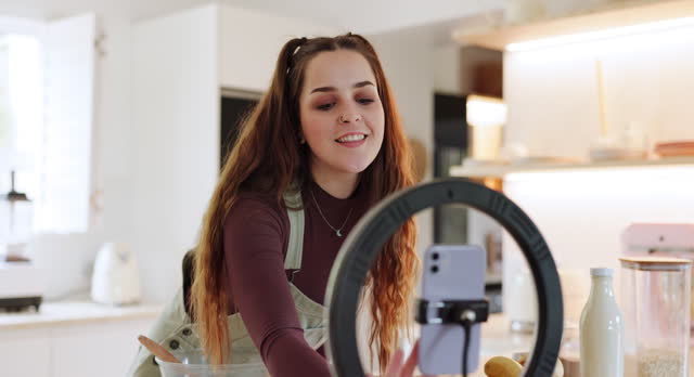 Woman, phone and live streaming in kitchen for cooking, food and meal blog for social media, vlog and website. Happy chef, lighting or home influencer with technology for baking broadcast tutorial