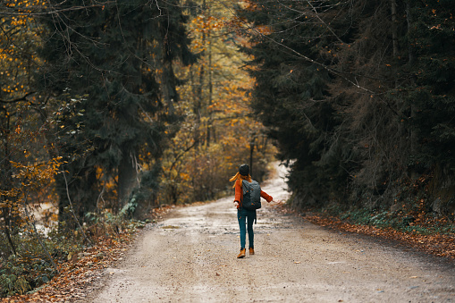 happy travel with a backpack in a warm sweater, trousers and boots walks along the road in the autumn forest. High quality photo