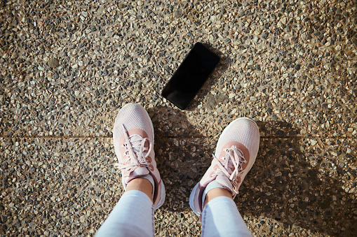 Sportswoman POV. Legs and feet of female athlete in stylish running sports shoes and smartphone with black blank mockup digital screen on the asphalt. Copy ad space for sports and fitness mobile app