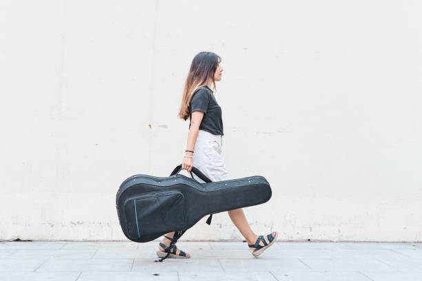 Caucasian woman carrying guitar case on sidewalk