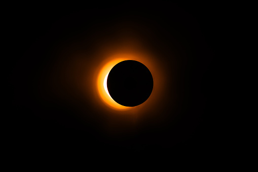 A large, glowing orange sun is in the center of a black sky. The sun is surrounded by a dark circle, which is the shadow of the sun. Concept of awe and wonder at the beauty of the sun