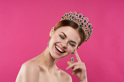 portrait of a woman with a crown on her head makeup decoration pink background. High quality photo