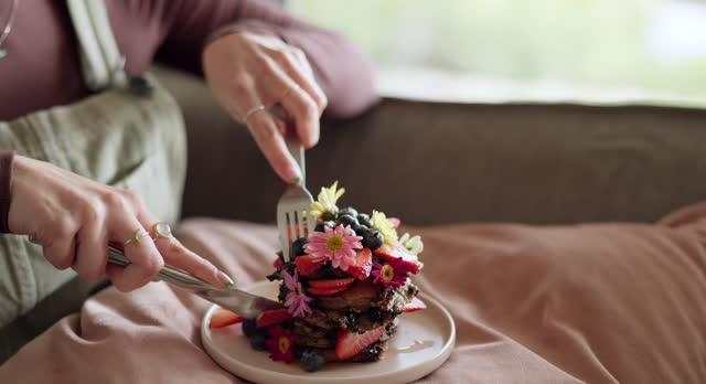 Woman, hands and eating cake for breakfast on birthday, morning in home to relax in living room with food. Cutting, knife and fork or person with dessert for meal on sofa in house on holiday or break