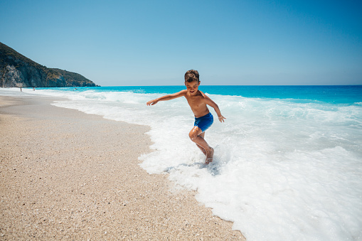 Boy enjoys playing with the waves on his summer vacation on the beautiful Greek Lefkada island