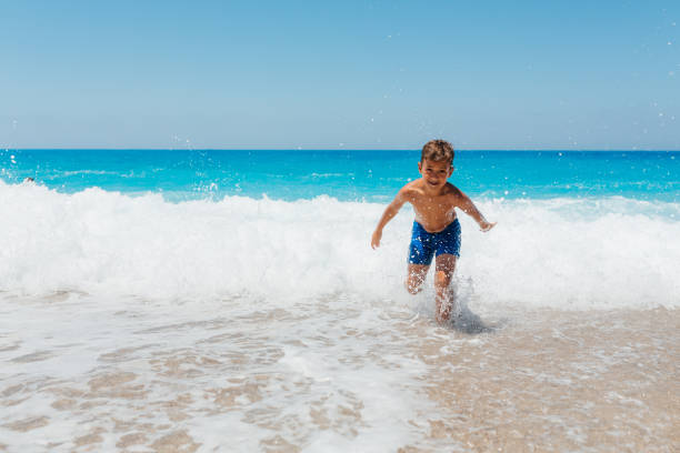 Boy enjoys playing with the waves on his summer vacation on the beautiful Greek Lefkada island