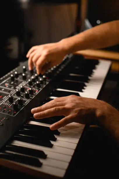 Photo of Focus on the foreground as a musician presses the keys of a professional synthesizer with one hand