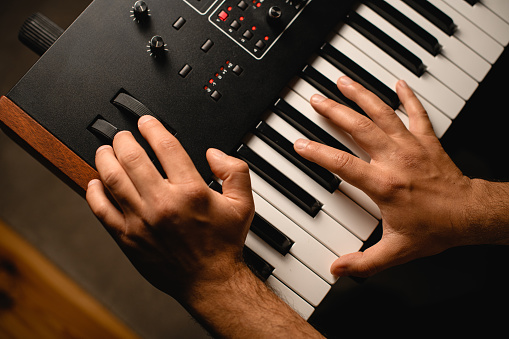 musician pressing the keys of a professional synthesizer with one hand and turning the equipment controls with the other hand in a recording studio