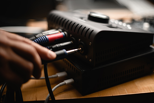 Close up side view of male hand inserting cable into jack of audio interface in recording studio, selective focus