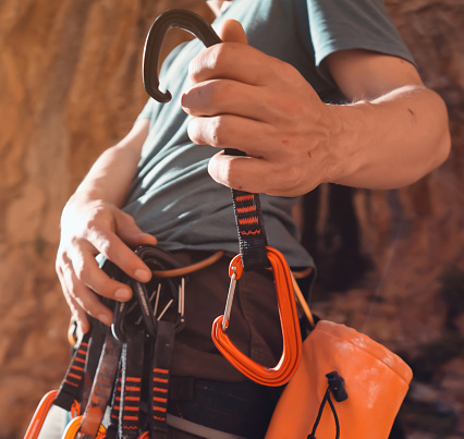 A young strong sporty man is engaged in rock climbing and mountaineering, a man's hand holds a climbing gear, a quickdraw close-up against a background of red rocks on a sunny day.