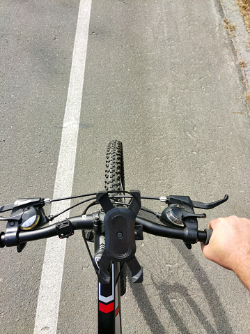 A top view of the handlebars of a bicycle riding on an asphalt road. A part of the hand on the steering wheel is also visible