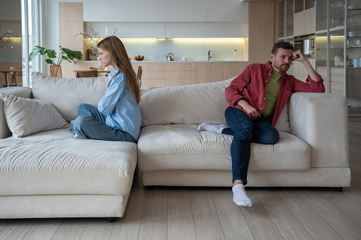 Unhappy couple having family problems sits on sofa at home, avoiding difficult conversation. Wife and husband not talking, resentful, ignoring, not satisfied with marriage. Unsuccessful relationships.