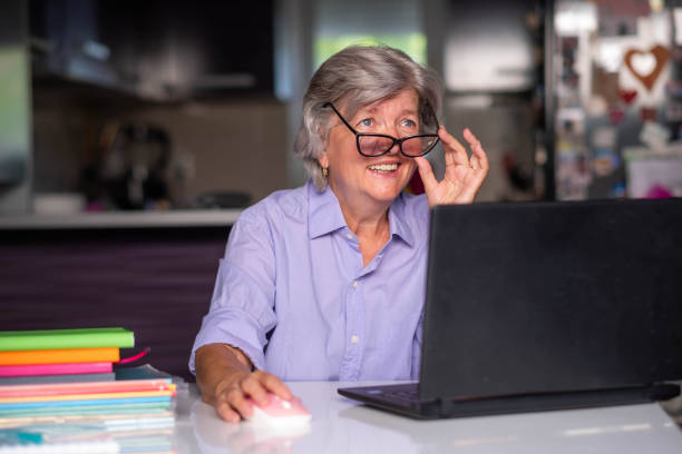 istock senior woman working at home using laptop, looking over glasses and smiling 2115697972