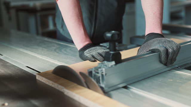 An unrecognizable craftsman with protective gloves uses an industrial circular saw