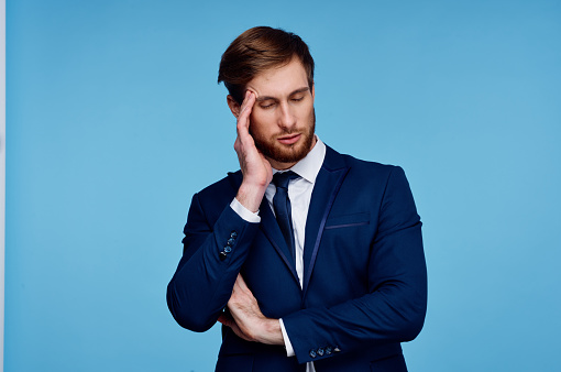 business man in a suit holds his hand near his head displeasure blue background. High quality photo