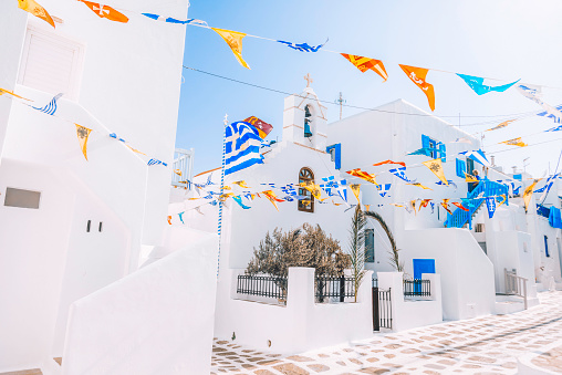 A traditional white and blue small, whitewashed alleys with flags of Mikonos town, Cyclades islands of Greece during sunny and windy summer day